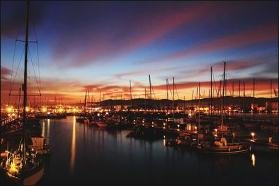 Sailboats moored at harbor against sky at sunset