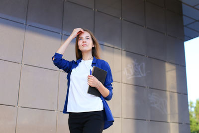 Portrait of young woman standing against wall