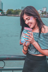 Woman holding illuminated string lights in jar against river