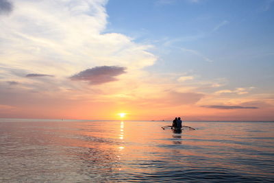 Silhouette people in boat on sea against sky during sunset