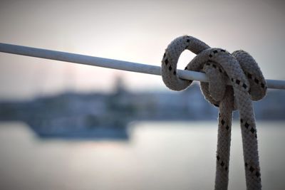 Close-up of rope tied on railing against sky