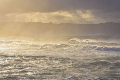 Big waves break on the coast, in the sunlit sea, passing through the clouds  sunset. galicia, spain.