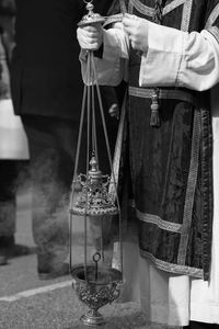 Midsection of priest holding metal while standing on road