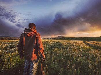 Rear view of man standing on field against sky during sunset