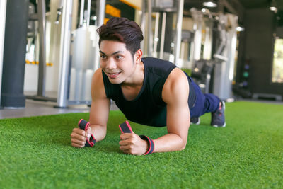 Smiling young man exercising on green carpet in gym