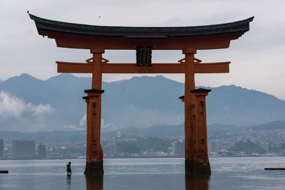 Man by huge torii gate in sea against mountains at itsukushima shrine