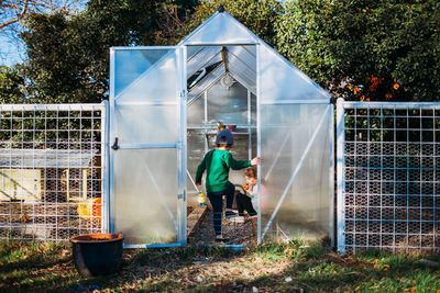 Young brother and sister sitting in backyard green house in spring