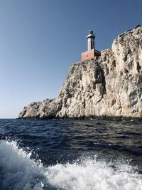 Lighthouse by sea against clear sky