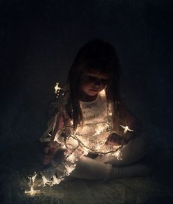 Cute girl with illuminated string lights against black background