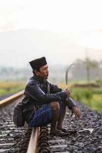 Man wearing hat sitting against sky