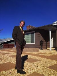 Low angle portrait of senior man standing outside house