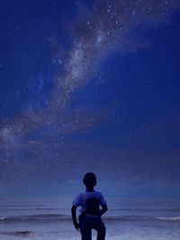 Rear view of boy standing by sea against sky at night