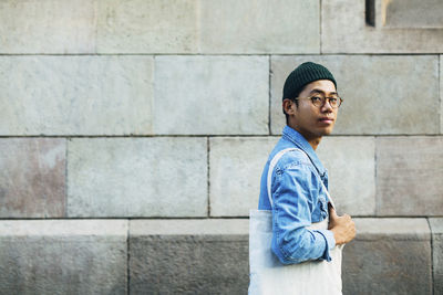 Side view portrait of man with bag against wall