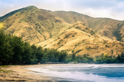 Scenic view of beach by mountains against sky