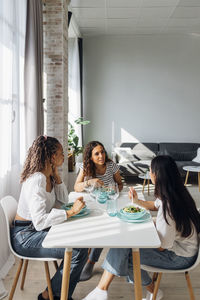 Young friends talking and having salad at dining table in living room