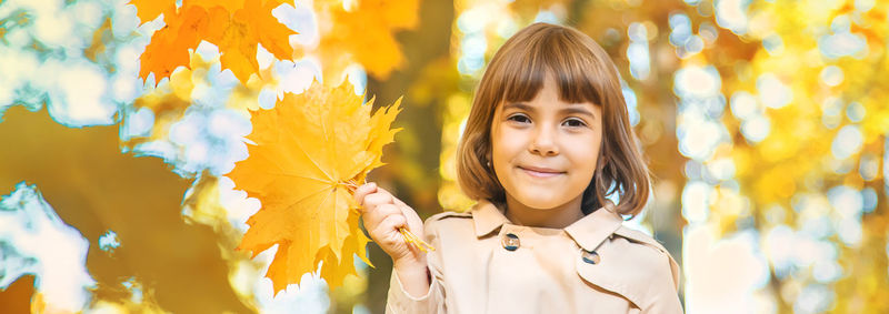 Portrait of girl holding maple leaves in forest