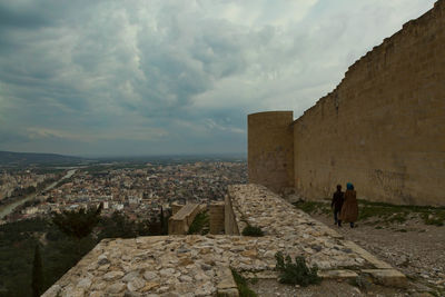 Rear view of people walking by historic building against cloudy sky at silifke