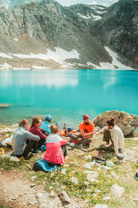 People sitting by lake against mountain