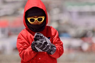 Boy in sunglasses and warm clothing holding snow outdoors