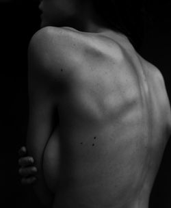 Rear view of shirtless woman standing against black background