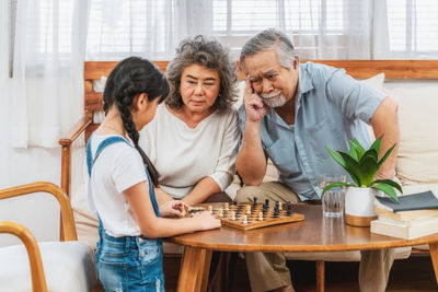 Cute girl playing chess with grandfather at home