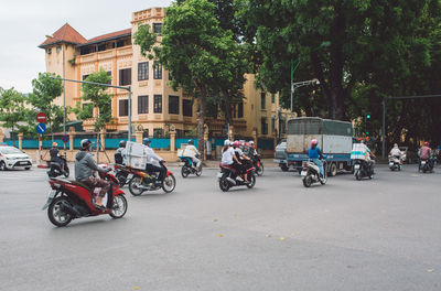 Rear view of people riding motor scooters on road in city