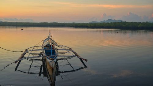 Outrigger canoe moored in river against sky during sunset