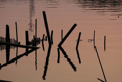 Silhouette wooden posts in lake against sky at sunset