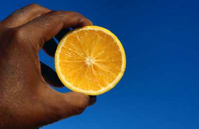 Close-up of man holding halved orange against clear blue sky