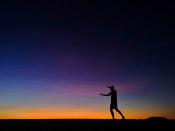 Silhouette man gesturing while standing on field against sky during sunset
