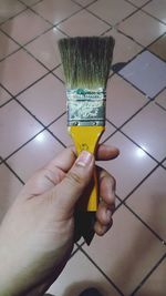 Cropped hand holding brush over tiled floor