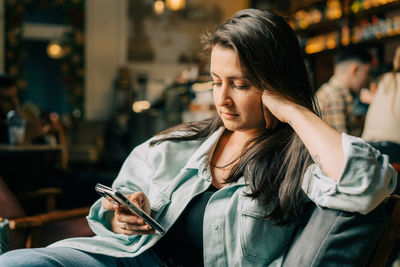 Hipster young woman reading text message on mobile phone at the cafe. person