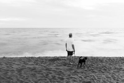 Real view of man with dog standing at beach against sky
