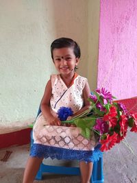 Smiling girl holding flower against wall