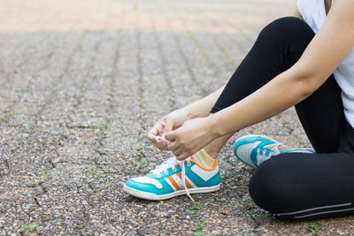 Low section of woman tying shoelace while sitting on street