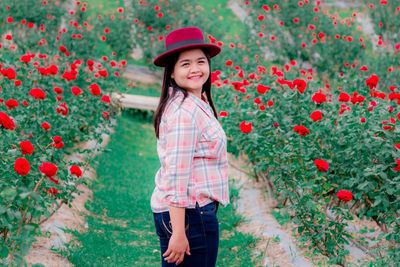 Portrait of smiling woman standing by red flowering plants