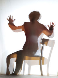 Shadow of woman on white fabric while sitting on chair