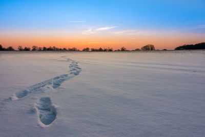 Snow covered landscape against sky during sunset