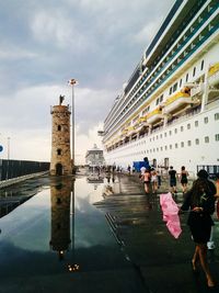 People walking on pier by cruise ship moored at harbor against sky