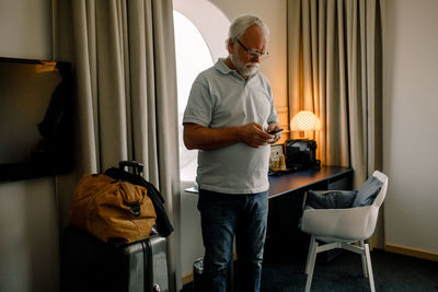 Senior man using smart phone while standing in hotel room