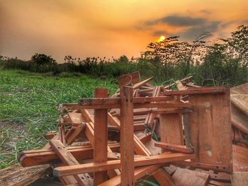 Wooden chairs on field against sky at sunset