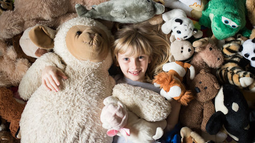 Directly above portrait of cute girl amidst stuffed toys at home