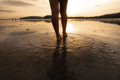 Low section of woman walking at beach during sunset