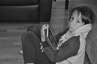 High angle portrait of boy sitting with digital tablet by sofa at home