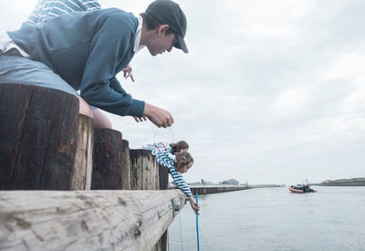 Children leaning over wooden railing to catch crabs from sea during summer