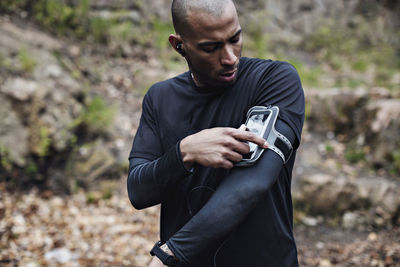 Male athlete using smart phone in arm band at forest