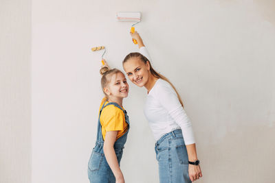 Beautiful and happy mom and daughter paint the walls in the apartment white.