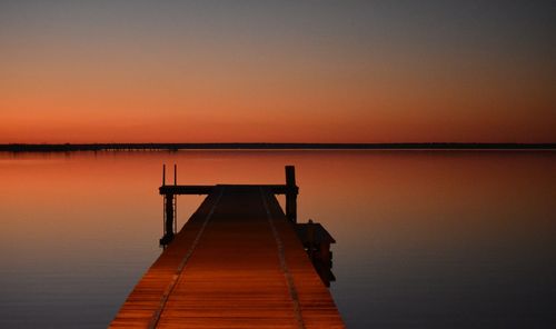 Pier over lake against orange sky