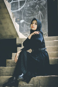 Portrait of woman sitting on staircase against building