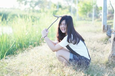 Side view of young woman holding stick on grassy field